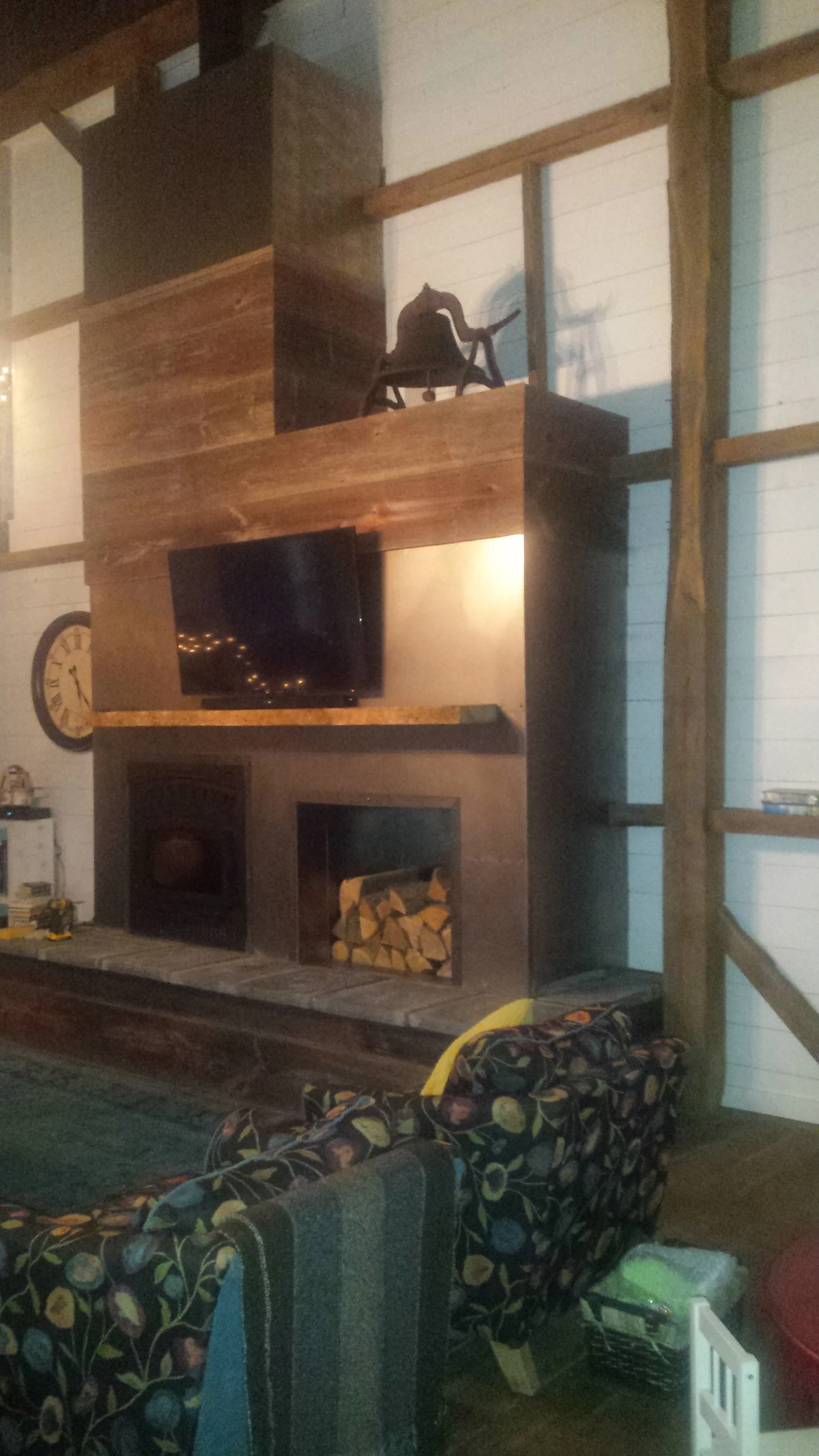 Completed fireplace surround clad in salvaged barn boards, with the dinner bell above