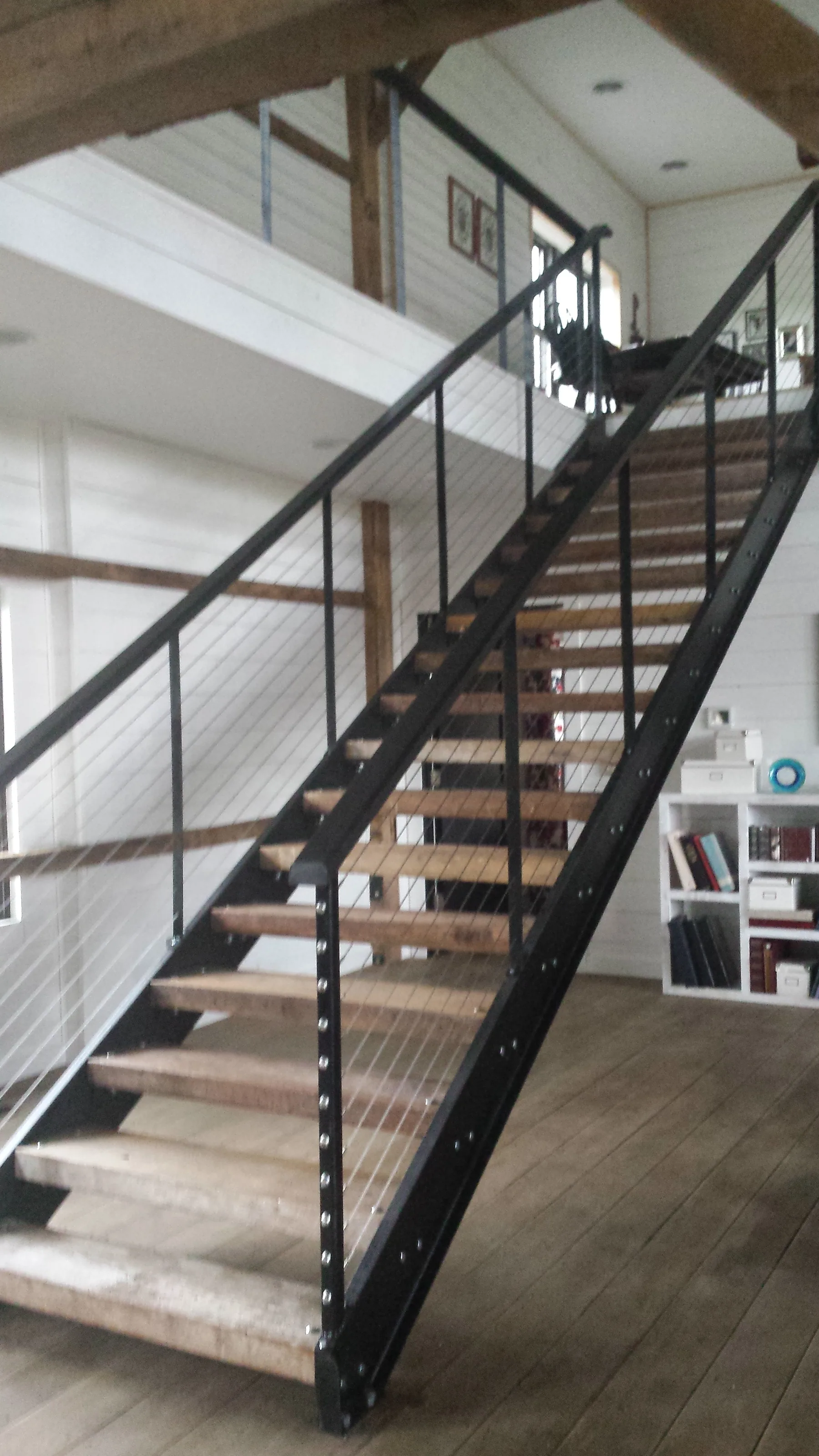 The finished staircase with barn-floor treads, channel-iron stringers, and cable railings